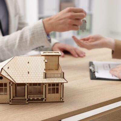 Real estate agent giving key to client at desk in office, focus on house model